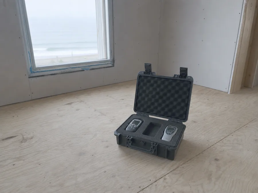 An open hard case of moisture measuring equipment on a bare floor, two meters seated in cut foam with one slot empty